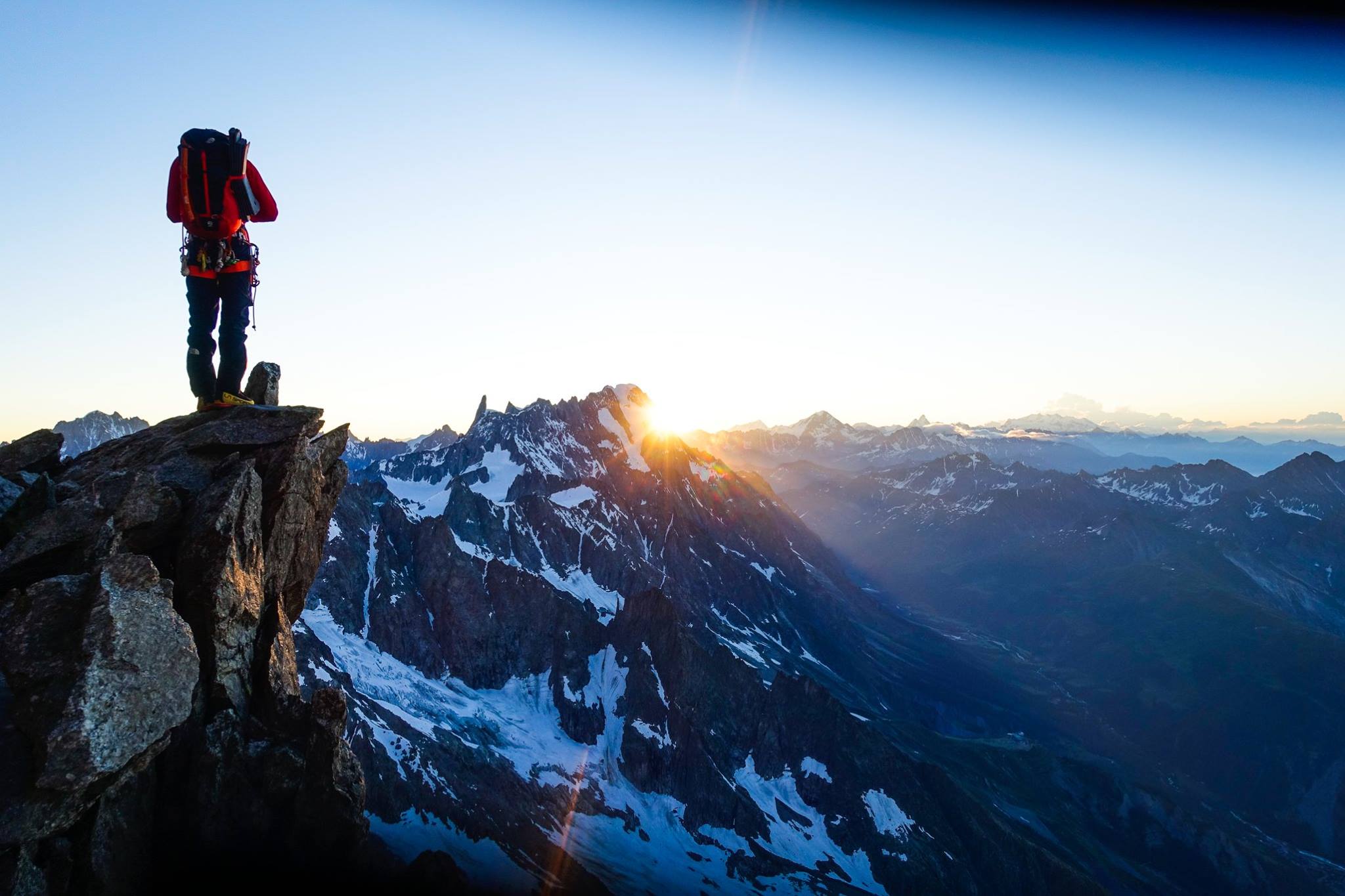 Panoramic view from a mountain summit — snow-covered peaks stretching to the horizon under a deep blue sky